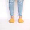 A woman wearing house slippers made of peach yellow and light gray wool felt