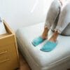 A woman wearing handmade house slippers made of turquoise blue and light gray wool felt slippers